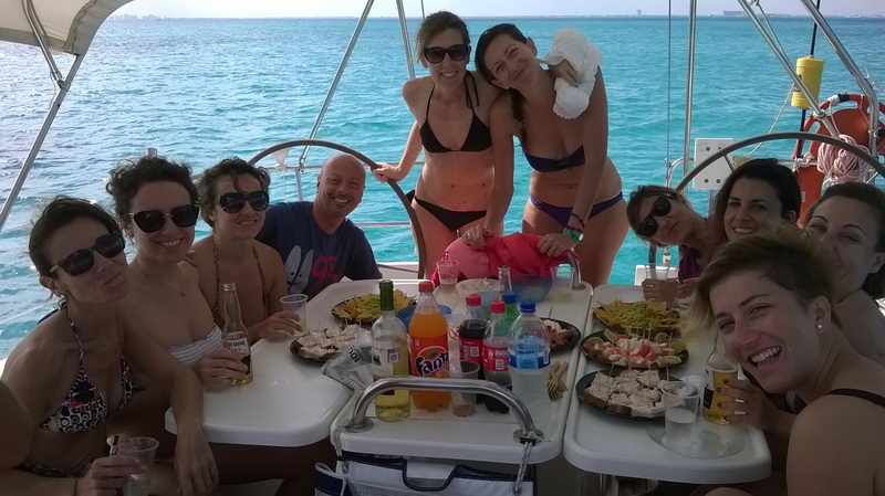 Happy group enjoying lunch with food and drinks on cockpit table of sailboat charter, private sailing party Caribbean Cancun