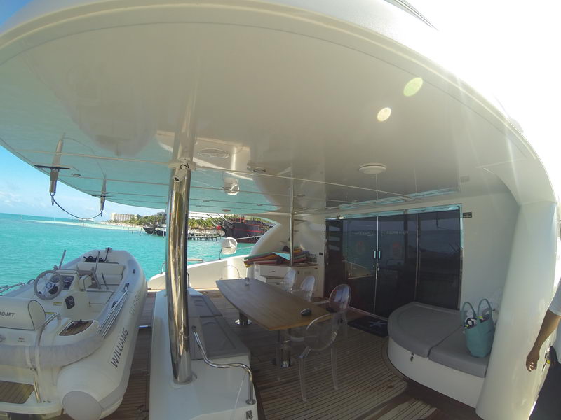 Shaded aft deck dining area with teak table and tender aboard the 66 ft Sunreef catamaran, luxury yacht charter Cancun